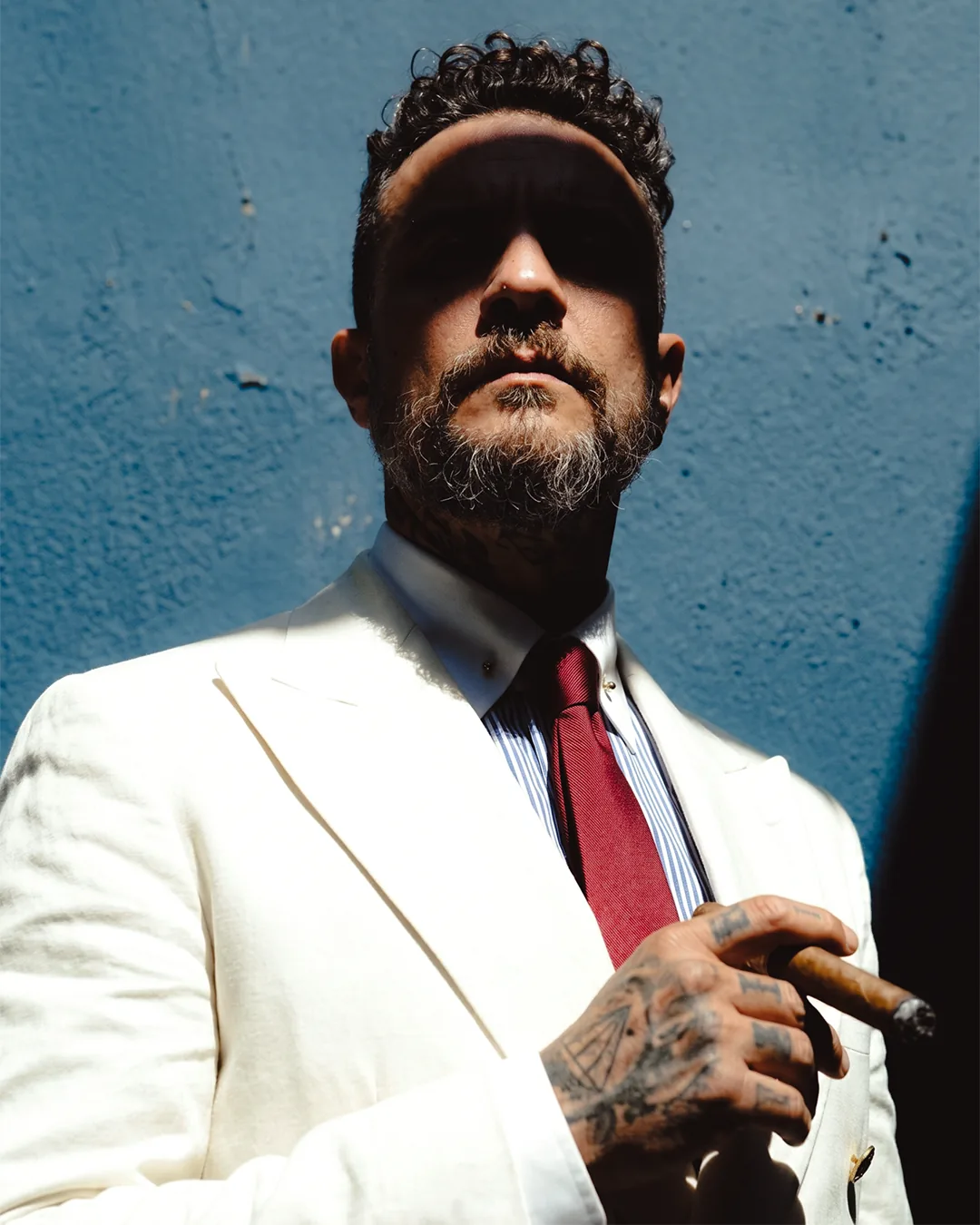 Portrait of a member in a cream suit and crimson tie holding a cigar