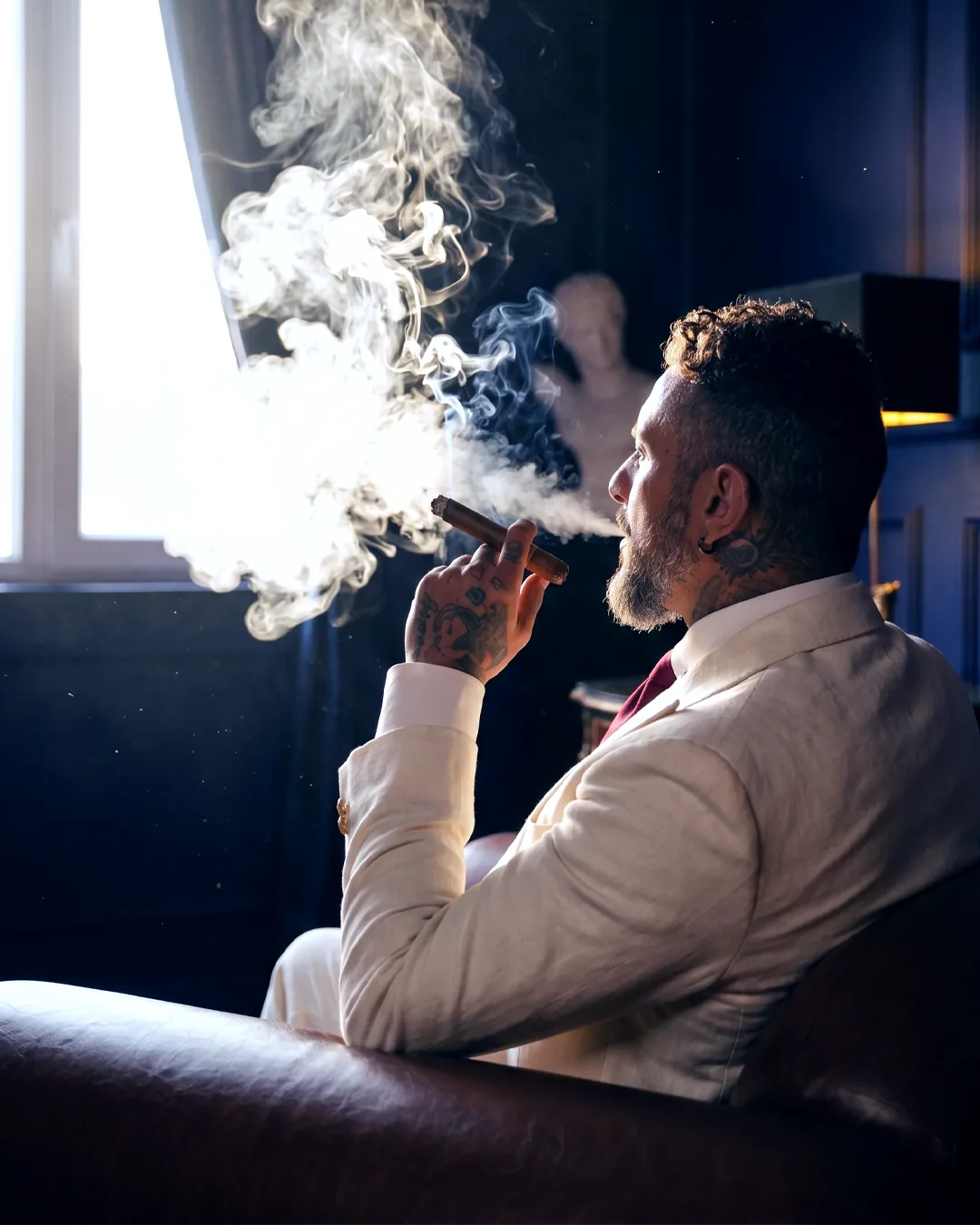 A member drawing on a cigar beside the lounge window, smoke curling in the afternoon light