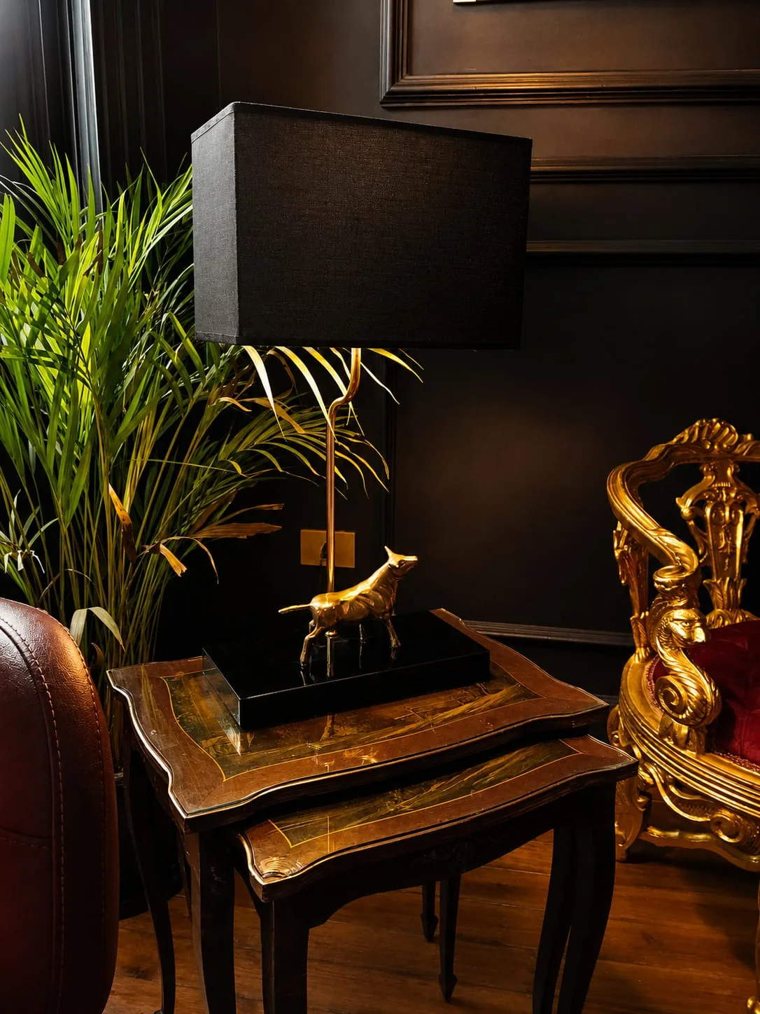 Brass lamp and inlaid nesting tables beside a gilded baroque armchair